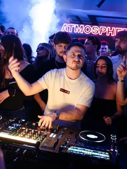 ASTR playing a club set, Atmosphere neon sign and crowd behind the booth